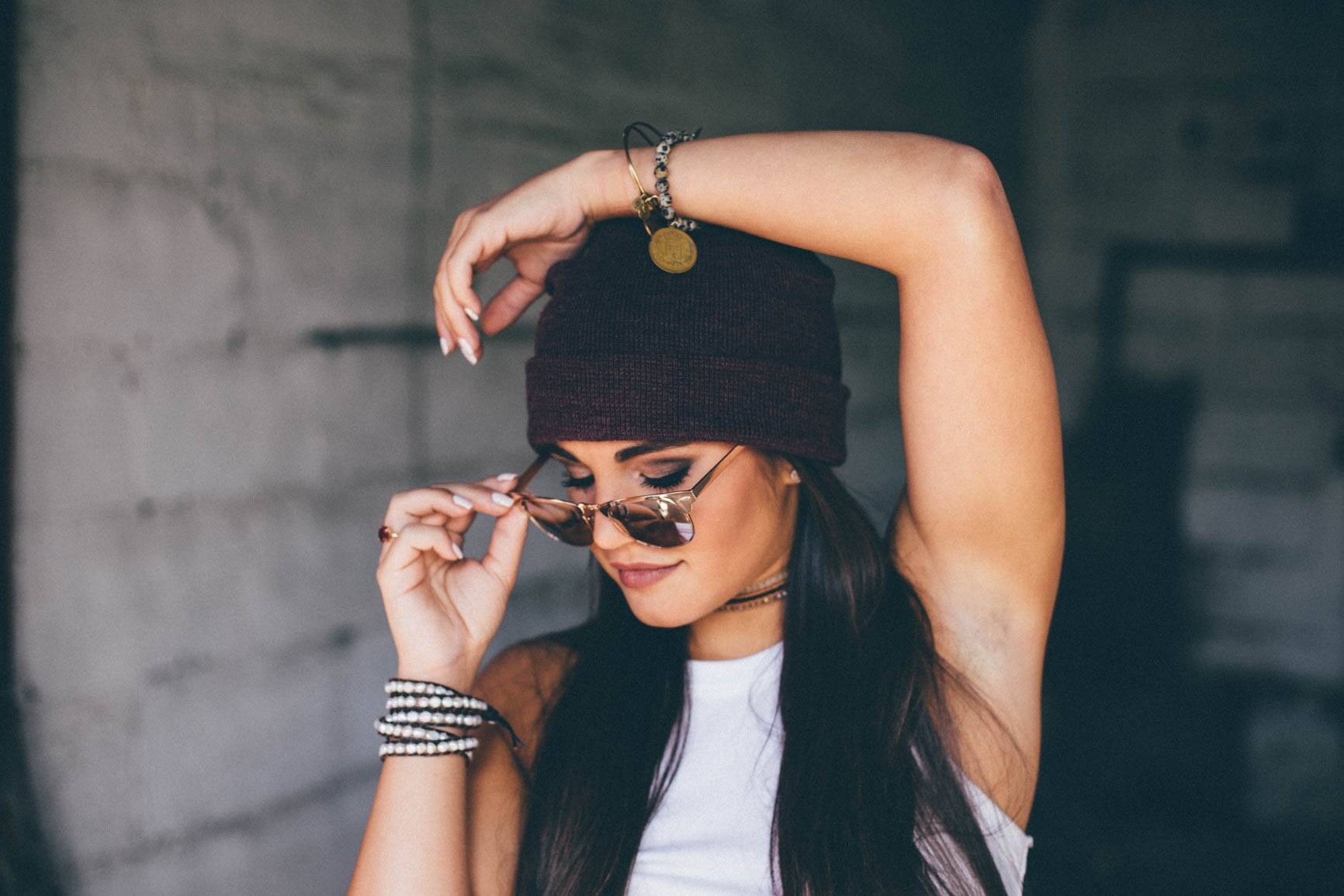 A young woman in a beanie holding her sunglasses with one hand